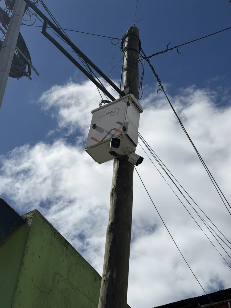 Dos cámaras de videovigilancia montadas bajo un gabinete blanco en un poste de madera, fotografiadas desde abajo contra el cielo.