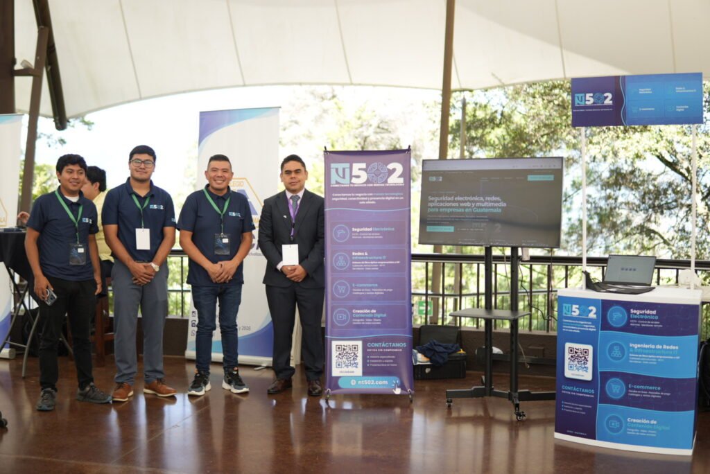Equipo de NT502 posando en su stand del Antigua Tech Summit 2026, junto a pendones con sus servicios y una pantalla que muestra el sitio web.