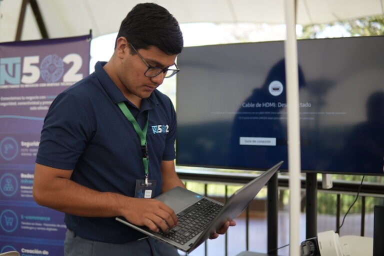 Integrante de NT502 con una laptop en el stand, junto a un pendón de NT502 y una pantalla.