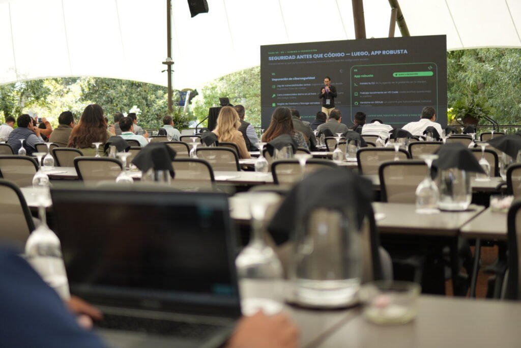 Charla «Seguridad antes que código, luego app robusta» vista desde el fondo del salón, con asistentes en las mesas.